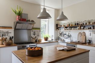 Cozinha espaçosa com prateleiras abertas e superfícies de trabalho em carvalho maciço. As luminárias pendentes e os móveis são ambos da Ikea