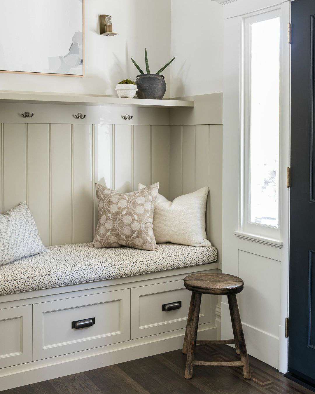 Um mudroom com banco de armazenamento embutido, uma almofada de banco e travesseiros decorativos.